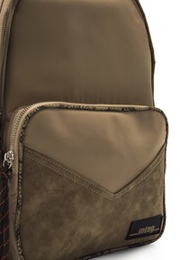 Sac à dos marron en nylon lisse et en suède, avec une poche à couture diagonale, une fermeture éclair et un détail de logo subtil.