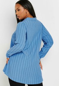 Maglia a maniche lunghe blu con texture a coste, collo alto, fessure laterali e vestibilità rilassata. Il tessuto è leggero e leggermente accorciato sul retro.