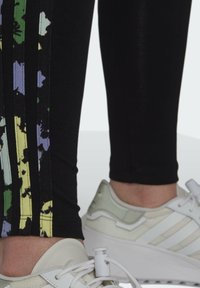 Mustat legginsit, joissa on monivärinen kukkakuosi sivuilla. Yhdistetty vaaleanvärisiin tennareihin, joissa on valkoiset raidat ja nauhat.