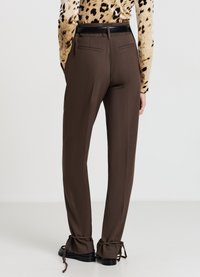 Pantaloni marroni su misura con una texture liscia, caratterizzati da una cintura nera, tasche posteriori e laccetti regolabili alle caviglie.