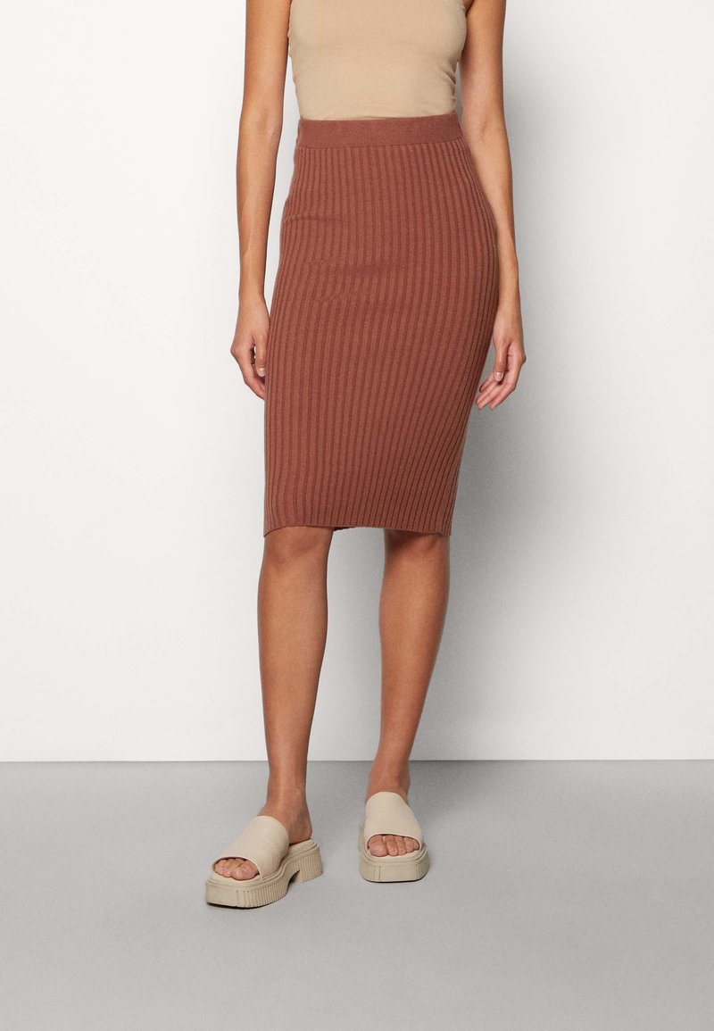 Jupe marron mi-longue à côtes avec une taille ajustée. Associée à des sandales à enfiler beige clair avec une semelle épaisse et texturée.