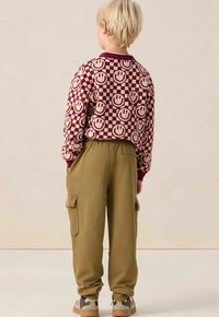 Sweatshirt maroon et beige à motif de visages souriants, associé à un pantalon cargo vert olive. Doté de poches latérales et de poignets côtelés.