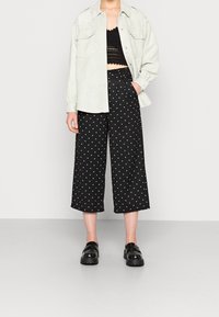 Jasnozielona zamszowa koszula, czarny koronkowy crop top, szerokie czarne spodnie culotte w białe groszki oraz masywne czarne buty.