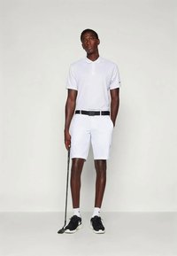 Polo alb cu guler, asortat cu pantaloni scurți albi. Curea neagră și adidași negri, ținând o rachetă de golf. Țesătură fină, design minimal.
