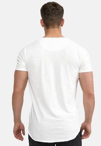 White short-sleeve t-shirt with a curved hem, made of a lightweight, textured fabric. Features a simple, minimalistic design and no visible patterns.
