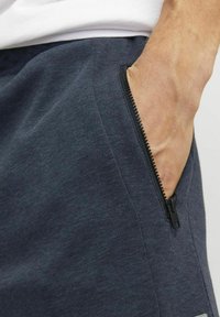 Donkerblauwe joggers van een gestructureerde stof, met een zichtbare zwarte ritszak, ontworpen voor comfort en functionaliteit.