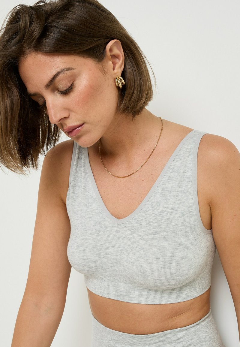Bralette grigia a costine con scollatura a V, caratterizzata da bordi in grigio chiaro a contrasto e un design senza cuciture, vista di lato con una texture morbida.