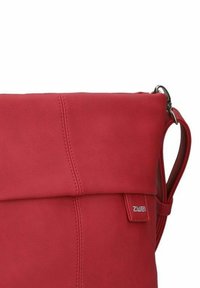 Borsa in pelle rossa con pattina pieghevole, texture liscia, tracolla regolabile e un piccolo etichetta con il logo sul lato.
