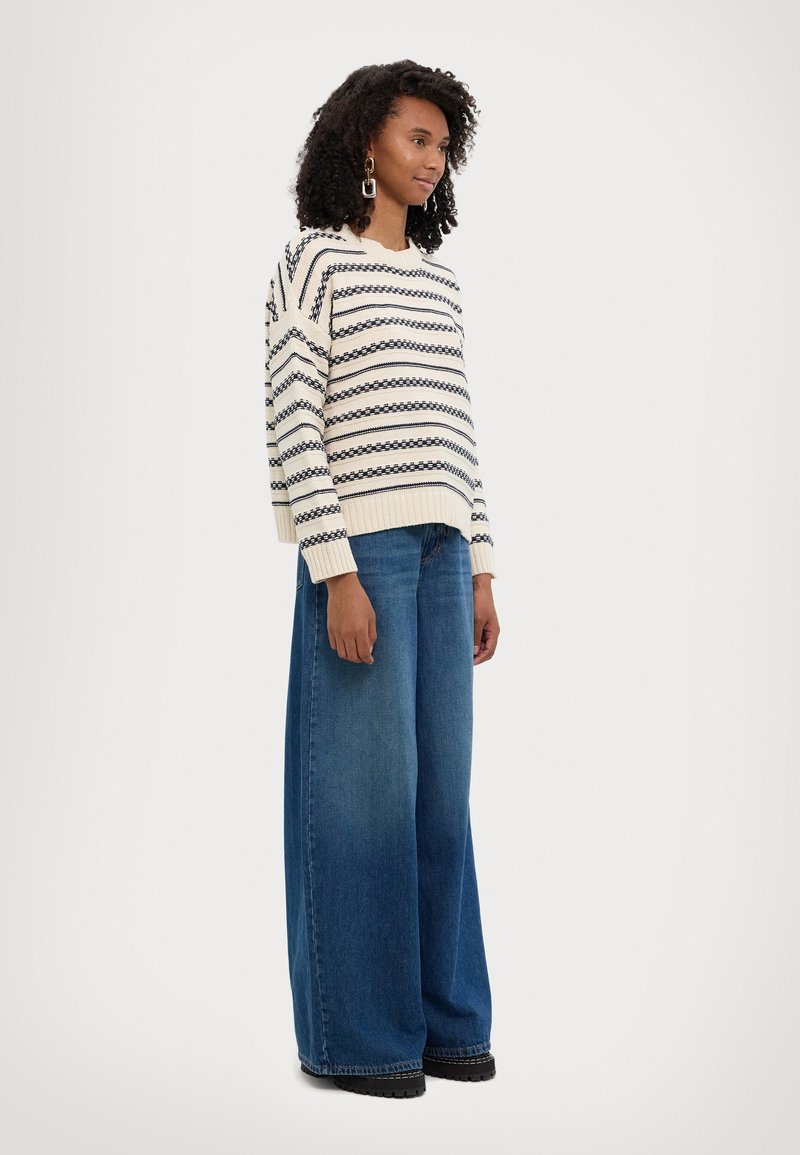 Maglione a righe in crema e blu navy, con polsini e orlo a costine. Abbinato a jeans in denim blu a gamba larga e stivali con tacco in nero.