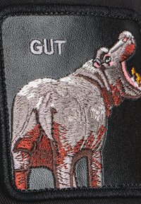 Parche bordado que presenta un hipopótamo gris con acentos rojos, sobre un fondo negro. Texto "GUT" en blanco encima del diseño.