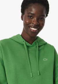 Hoodie verde in cotone con cappuccio regolabile e logo ricamato sul petto. Tessuto morbido con vestibilità comoda e maniche lunghe.