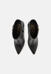 Μαύρα δερμάτινα μποτάκια αστραγάλου με μυτερή μύτη, που διαθέτουν διπλές φερμουάρ πλάι και χρυσή λεπτομέρεια στη φτέρνα, λεία επιφάνεια και μινιμαλιστικό σχέδιο.