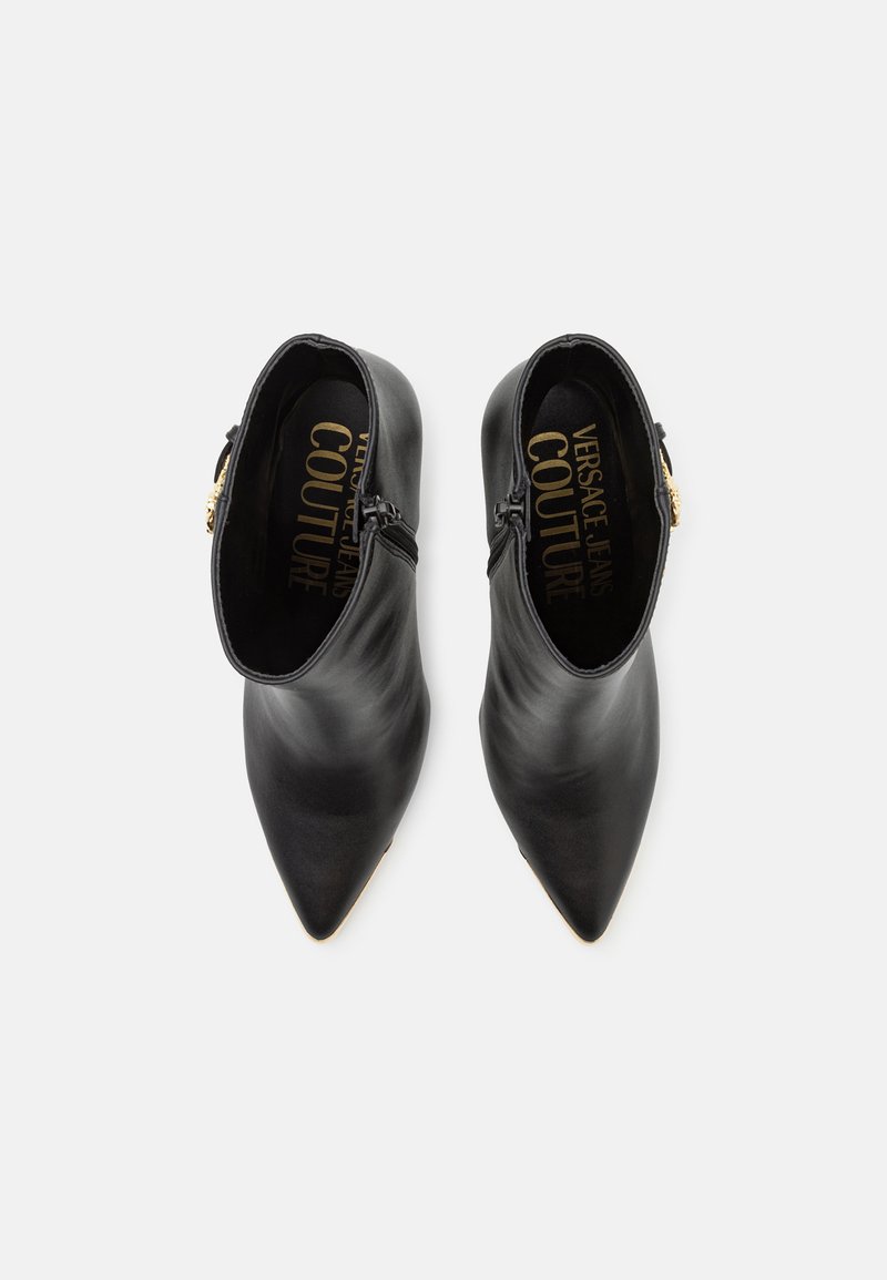 Stivali neri in pelle a caviglia con punta appuntita, dotati di doppie cerniere laterali e un'accenno dorato sul tacco, superficie liscia e design minimalista.