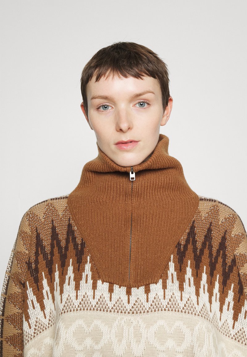 Brauner, gerippter Pullover mit hohem Kragen und geometrischen Mustern in Beige und Dunkelbraun. Verfügt über einen halben Reißverschluss an der Vorderseite und ein strukturiertes Strickdesign.