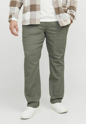 Olive green trousers with a straight cut, smooth texture, and belt loops, paired with white sneakers and a checked shirt above.
