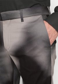Byxor i gradientnyanser av grått, tillverkade av mjukt tyg. Har en slim fit, framfickor och ett elegant bälte som matchar midjebandet.