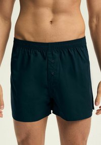 Granatowe szorty kąpielowe wykonane z lekkiego materiału, z elastycznym paskiem w talii, dwoma przednimi guzikami oraz bocznymi rozcięciami dla większej swobody ruchów.