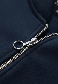 Tessuto di felpa blu scuro con un primo piano di una cerniera argentata dotata di un tira zip rotondo, che mette in evidenza una consistenza liscia e cuciture raffinate.