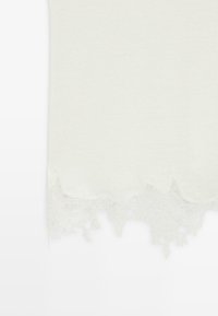 Weißer Stoff mit zarter Spitzenverzierung mit floralem Muster entlang des unteren Randes.