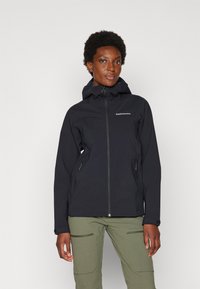Veste imperméable noire avec capuche, fermeture éclair sur le devant et poches latérales. Présente un design élégant et est associée à un pantalon vert.