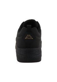 Chaussure de sport noire avec une semelle en caoutchouc texturé, un dessus en maille et un accent de logo doré au niveau du talon. Dotée d'une languette pour un enfilage facile.