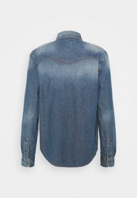 Camicia di denim blu medio con finitura sbiadita, polsini con bottone e colletto a punta. Presenta una gioga sul retro e un orlo arrotondato.