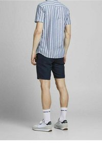 Kortärmad skjorta med blå ränder och bakstycke, kombinerat med mörka shorts. Vita strumpor och ljusa sneakers fullända outfiten.