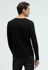 Black long-sleeve sweater with a textured knit pattern. Features a crew neck and a straight hem, shown from the back over dark jeans.
