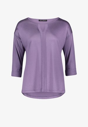 Blouse pour femme lilas à manches trois-quarts, col rond avec une petite encoche centrale, et un panneau vertical cousu sur le devant.