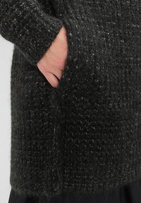 Dark gray knit sweater with a textured finish, featuring a side pocket and a relaxed fit, made from a soft, fuzzy material.