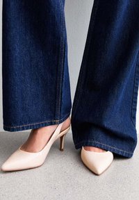 Décolleté in vernice color carne con punta affusolata e tacchi a stiletto da 5 cm, abbinati a jeans in denim scuro a gamba larga.