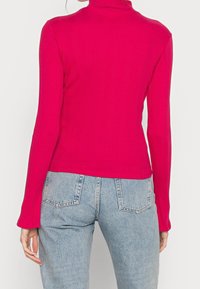 Åtsittande, rippad polotröja i starkt rosa med långa ärmar och rak nederkant, tillsammans med högmidjade ljusblå jeans.