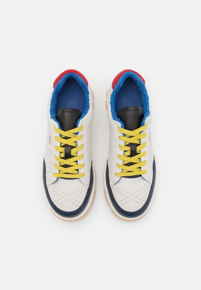 Baskets en cuir blanc avec des accents navy, des lacets jaunes et une doublure en feutre bleu. Langue noire et détail rouge au talon. Côtés perforés pour la respirabilité.