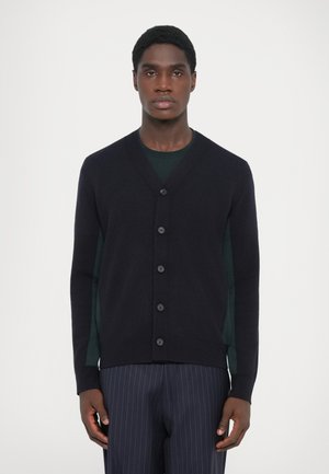 Navy wool cardigan with a V-neck, featuring six buttons down the front and long sleeves, paired with a dark green shirt underneath.