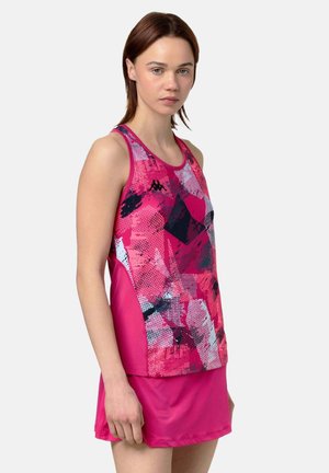 Giovane donna che indossa un top sportivo rosa senza maniche con fantasia e una gonna rosa abbinata, in piedi su uno sfondo chiaro.