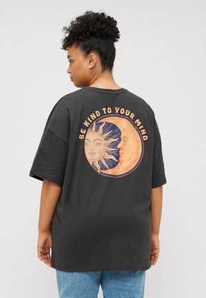 Sort oversized t-shirt med et grafisk design af en sol og måne på ryggen, med teksten "VÆR VENLIG MOD DIN HJERN" i orange.