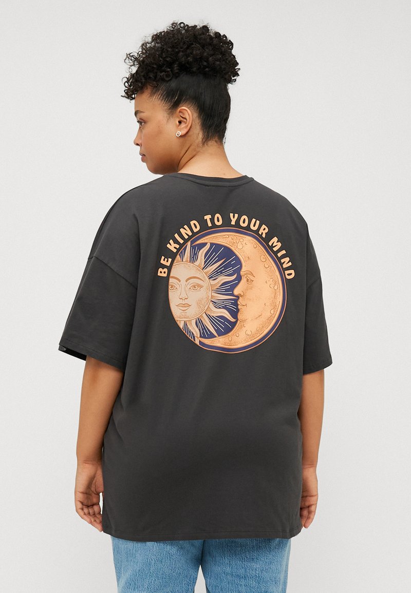 Schwarzes, übergroßes T-Shirt mit einem grafischen Design von Sonne und Mond auf der Rückseite, mit dem Text "SEI NETT ZU DEINEM GEIST" in Orange.