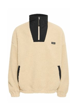 Fleece pullover in beige with a black zippered collar and side pockets, textured surface, and elastic cuffs for a snug fit.
