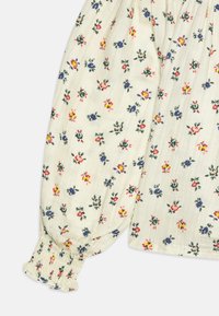 Blusa di tessuto bianco con stampa floreale multicolore, dotata di polsini elasticizzati e una consistenza morbida e leggera. Design con collo rotondo.