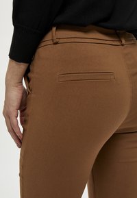 Smeđe uske hlače od rastezljivog materijala, sa ravnim stražnjim džepom i glatkom teksturom, s visokim strukom.