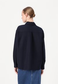 Navyblauwe oversized shirt van gladde stof, met een klassieke kraag en knoopsluitingen aan de mouwen, gezien van de achterkant.