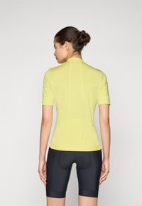 Kortermet sykkeltrøye i lys gul, laget av pustende stoff med en tettsittende design. Kombinert med svarte sykkelshorts.