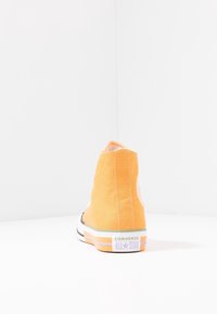 Baskets montantes Converse All Star jaunes vues de dos sur une surface blanche et avec un fond blanc.
