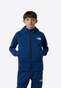 Tengerészkék, cipzáros kapucnis pulóver, puha anyagból. Bal mellrészen logóval, két kéz zsebbel. Simogató tapintású felület.