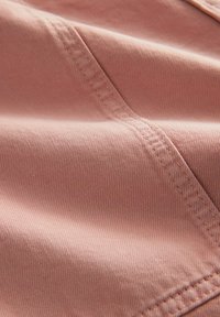 Gros plan sur un tissu rose avec une couture diagonale visible et des points détaillés, montrant une texture lisse et de légers plis.