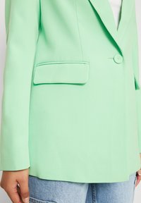 Myntgrønn blazer laget av glatt stoff, med en enkel knappelukking og en brystlomme. Løs passform med lange ermer.