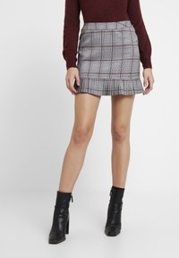 Jupe mini à carreaux gris avec une bordure volante, dotée d'accents noirs et rouges. Portée avec des bottines noires, mettant en valeur le tissu texturé.