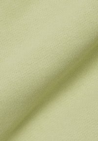 Primo piano di tessuto lavorato a maglia verde chiaro che mostra una trama fine e liscia e sottili pieghe diagonali.