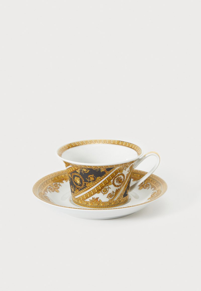 Porcelænskop og underkop med udsmykket guld- og sort design, der indeholder indviklede mønstre og et buet håndtag. Glat, blank finish.