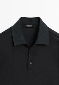 Schwarzes Poloshirt, geripptes Material, kurze Ärmel, flacher Kragen, Knopfleiste mit drei Knöpfen, "Massimo Dutti"-Label im Nacken.